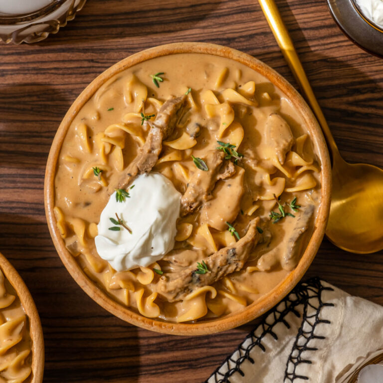 A bowl of beef stroganoff made with Ronzoni® egg noodles topped with a dollop of sour cream and a sprinkle of thyme.