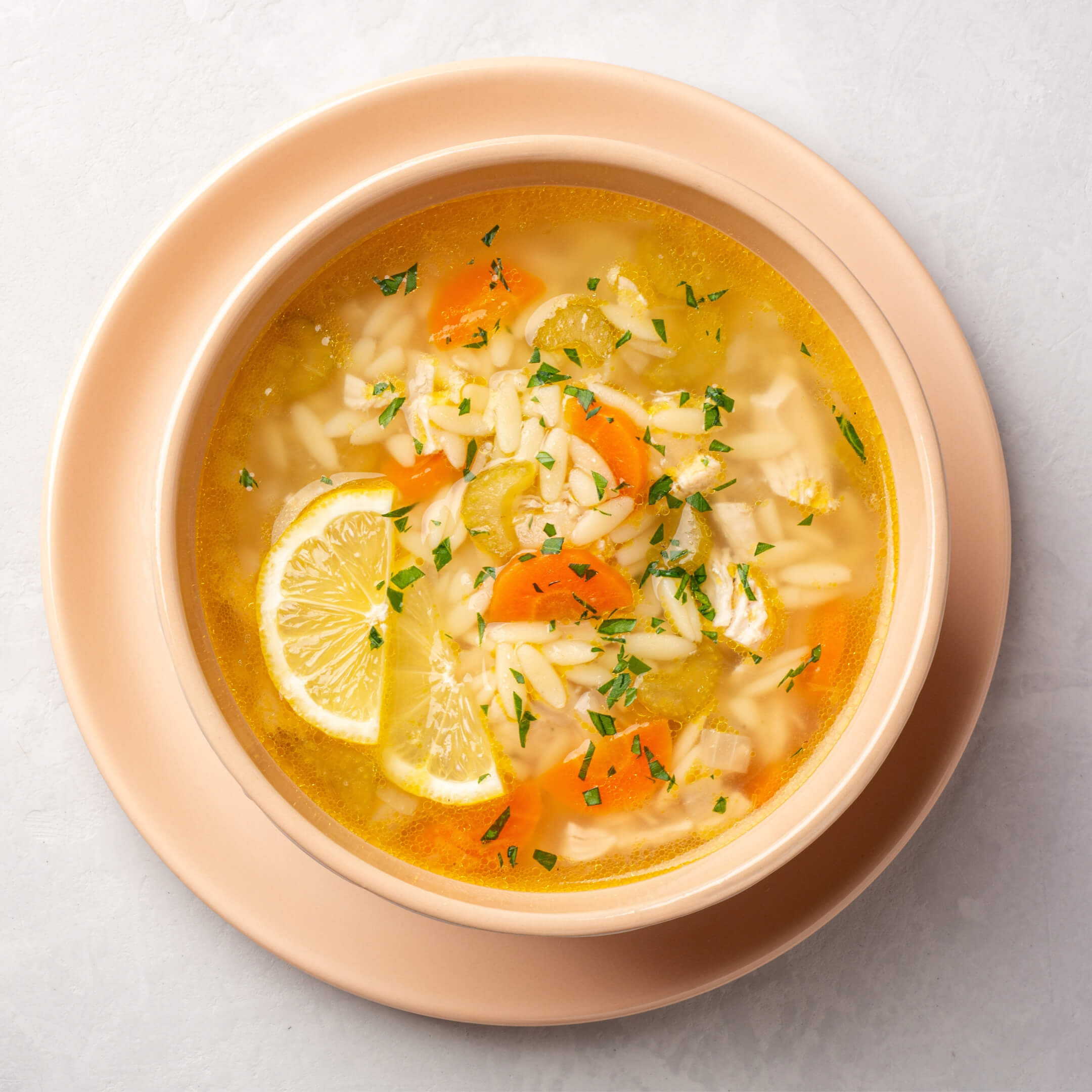 bowl of lemony chicken soup with orzo and vegetables in broth