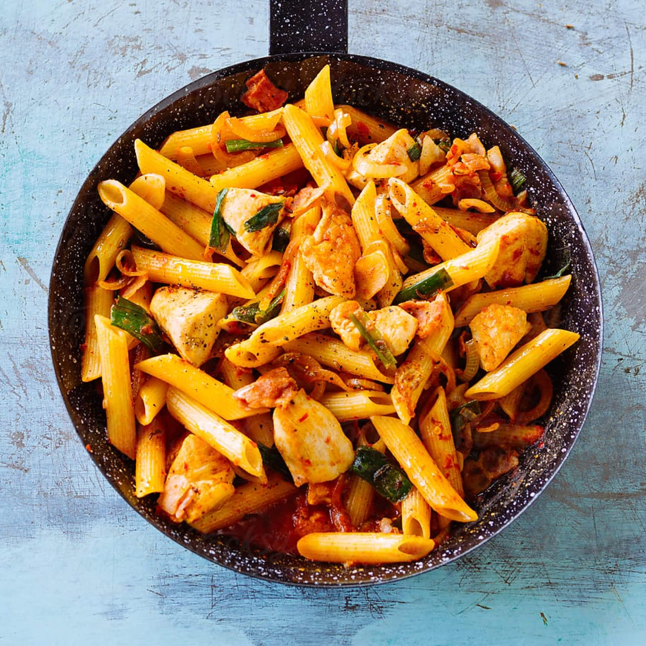 grilled chicken and penne pasta in skillet with vegetables and tomato sauce