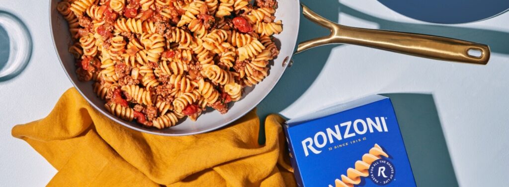 Short pasta in skillet next to Ronzoni packaging