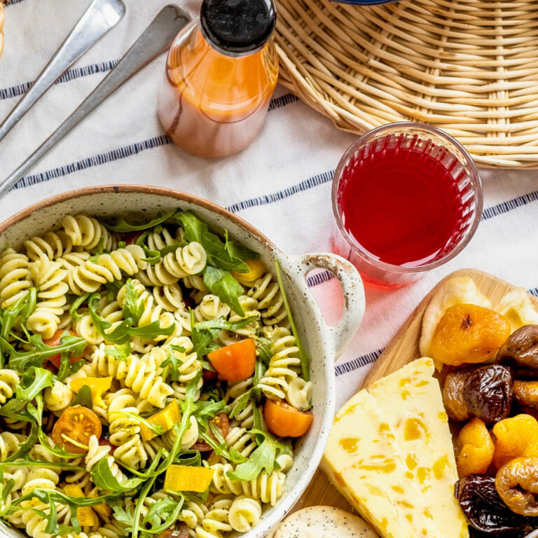 Swirly, twirly pasta salad on a picnic blanket next to other snacks, drinks and sauces.