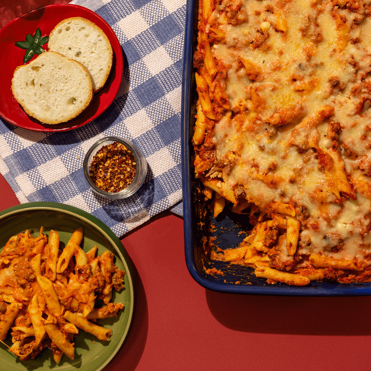 Overhead view of mostaccioli dish next to plate and bread