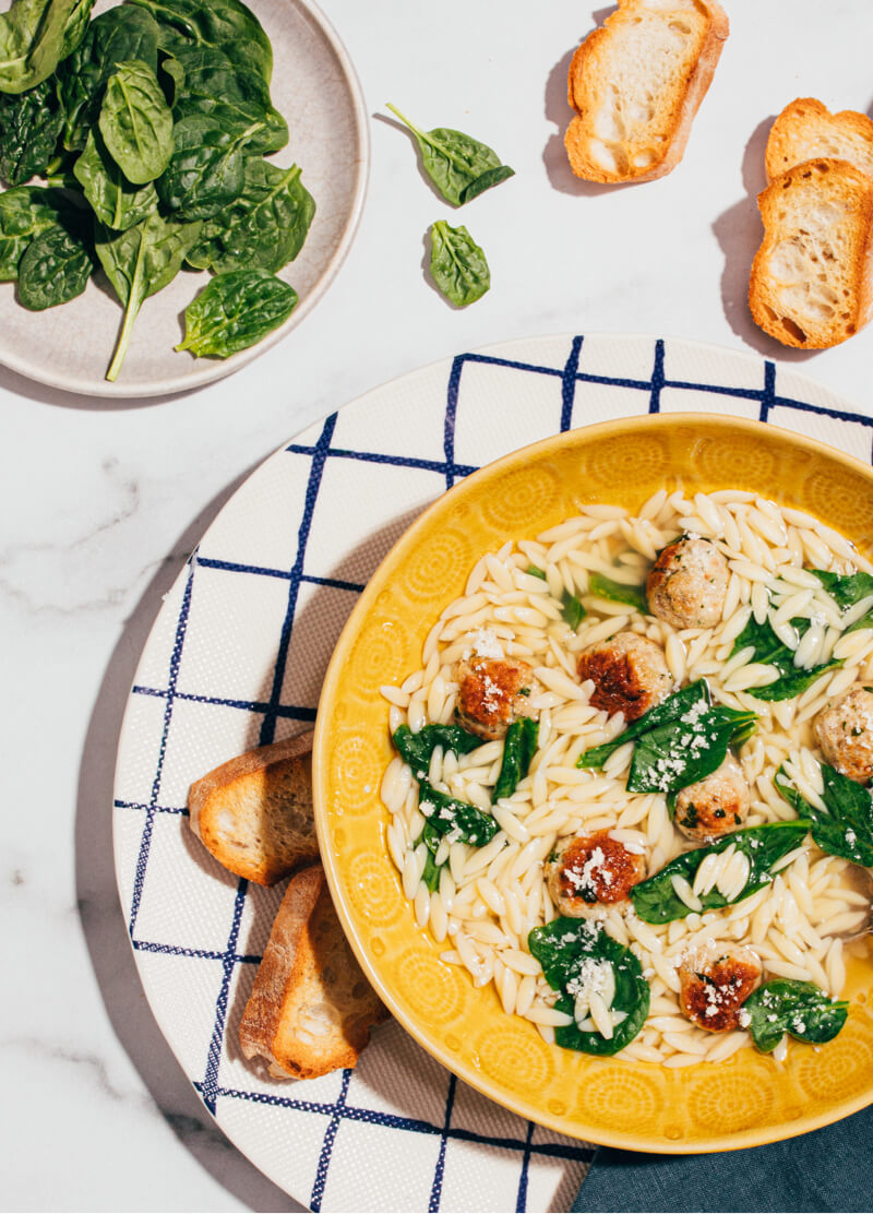 One of our best winter pasta recipes: a bowl of Italian Wedding Soup, surrounded by toasted bread and spinach.