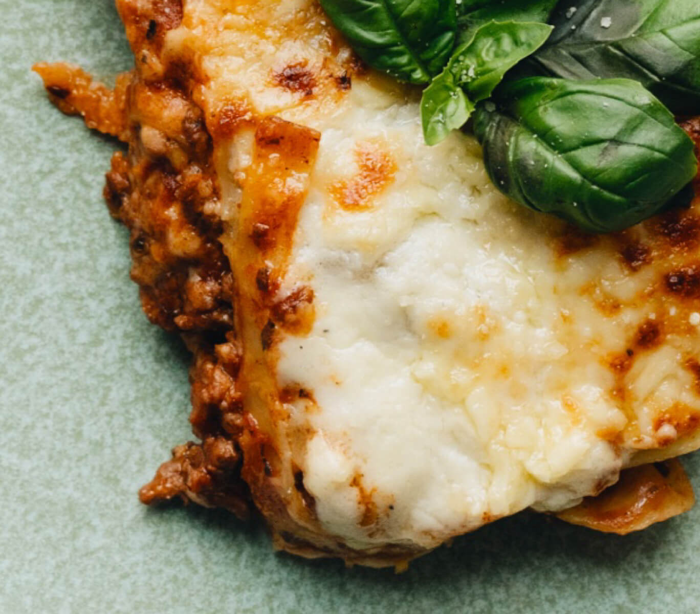 Close up of Ronzoni’s Easy Oven-Ready Lasagna on a plate with utensils and fresh basil.